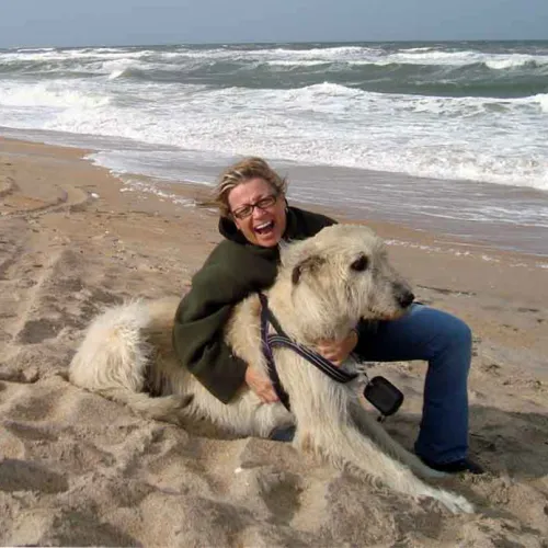 Wheaten wolfhound and very happy woman on the beach with ocean behind them