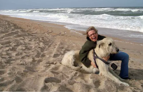 Wheaten wolfhound and very happy woman on the beach with ocean behind them